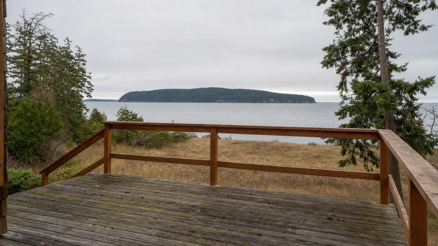 A deck and railing on an island property overlooking calm water and a forested island
